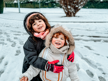 Two children wearing insulated snowsuits smiling together in a snowy outdoor environment, showcasing warmth, comfort, and protection for winter adventures.